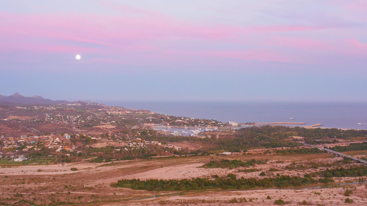 Moon above coastal town and dry fields at twilight