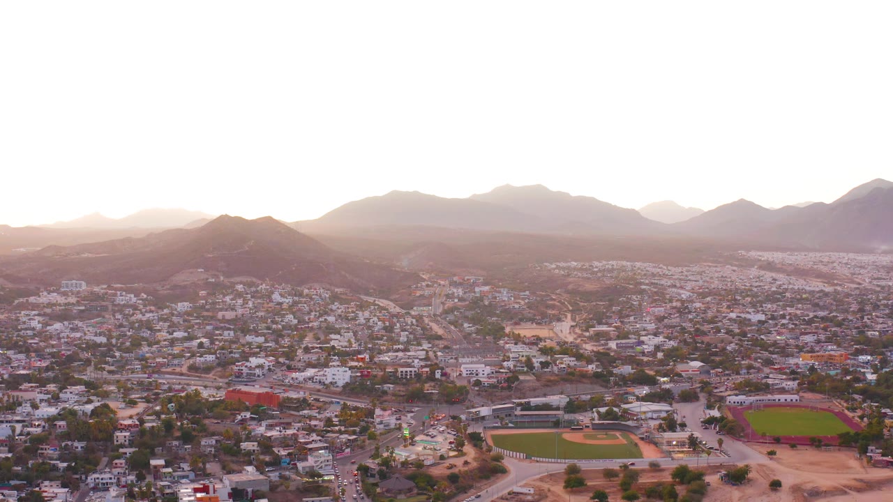 Wide drone view of city blocks, fields, hills, and mountains.
