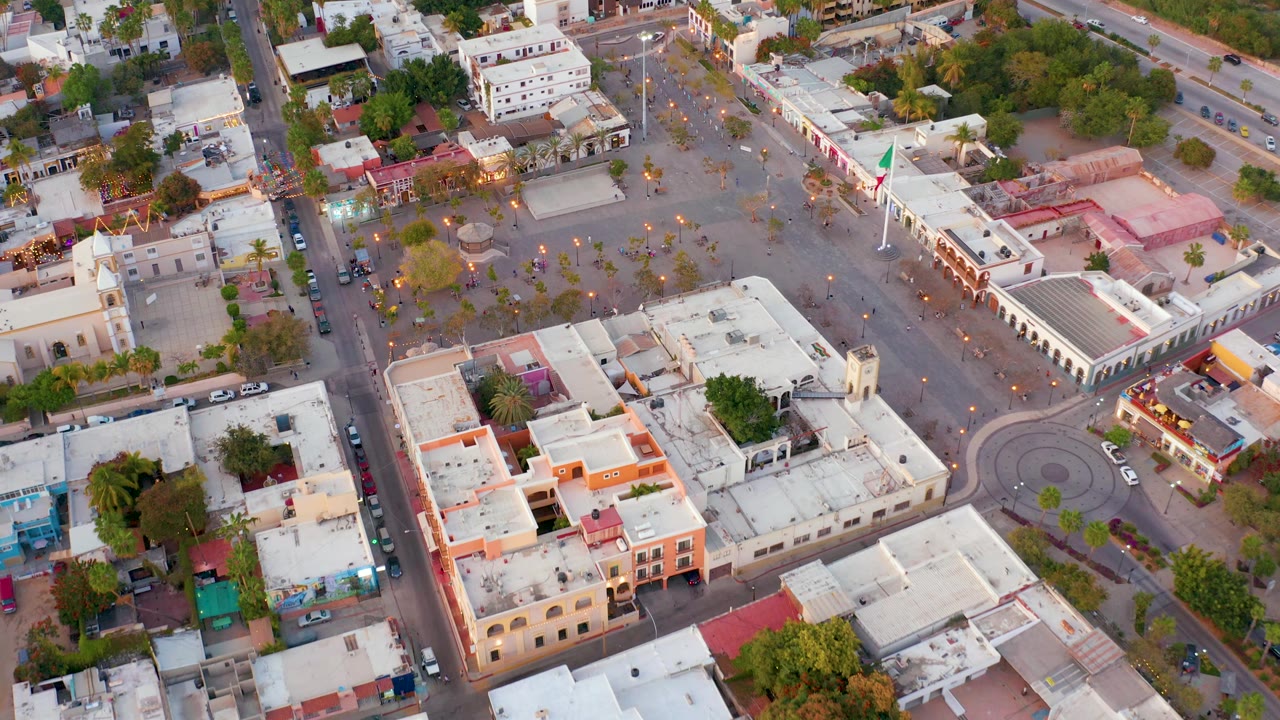 Closer aerial of plaza paving, flagpole, trees, buildings, and cars on streets.