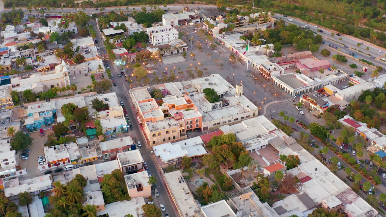 Overhead town view with a central paved space, roads, trees, and low-rise buildings.