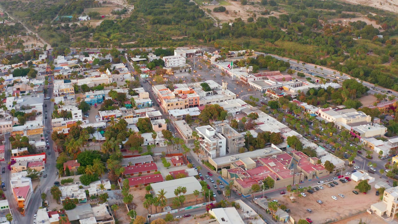 San Jose del Cabo aerial view with a diagonal main road at right, compact town buildings, parking lots, red roof sections, palms, and no visible people.