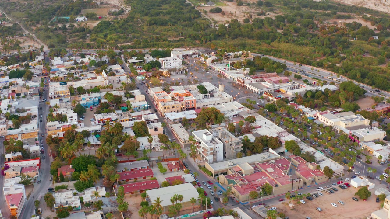High aerial town view with roads, parked cars, red roofs, and trees.