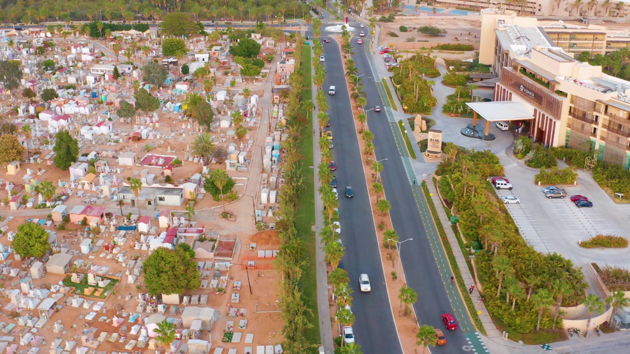 Aerial view of roadway traffic beside a large building and dense settlement.