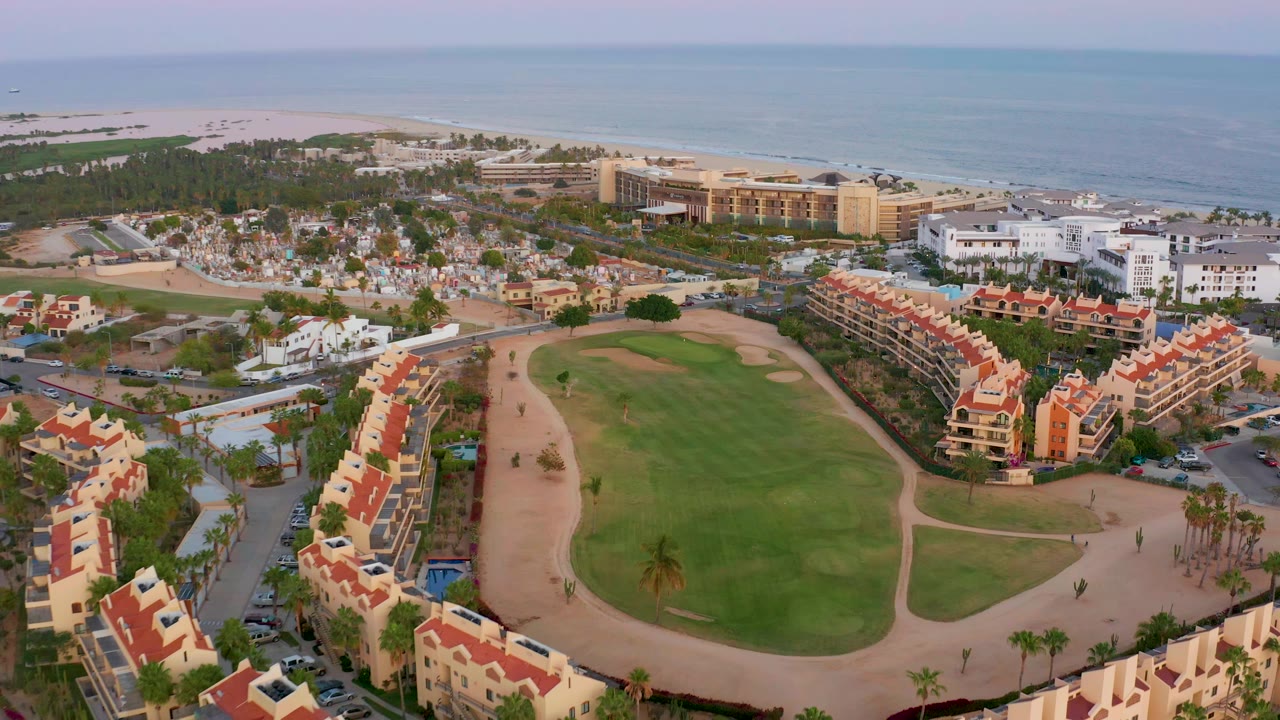 Wide aerial over resort buildings, golf course, beach, and ocean