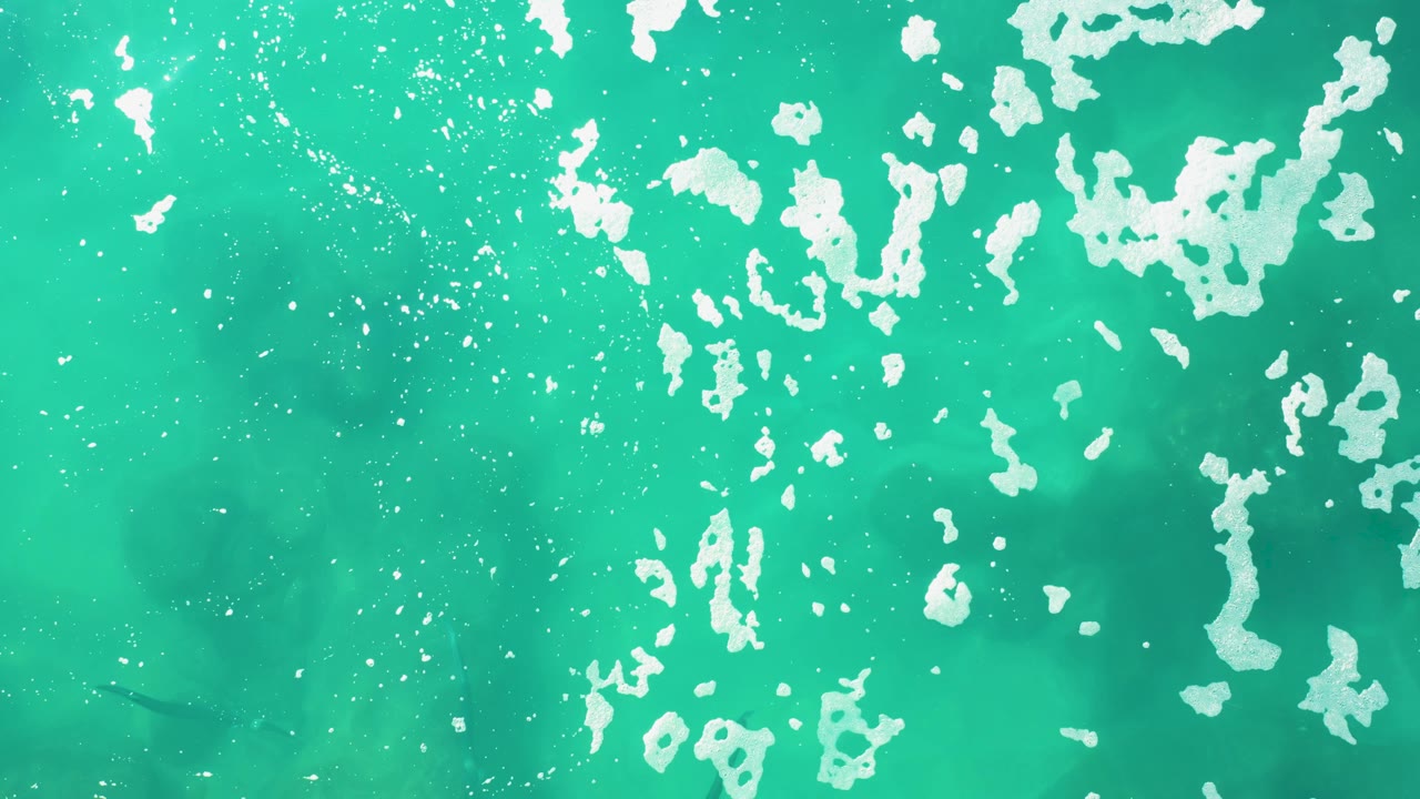 Turquoise ocean water with white foam and fish shadows below