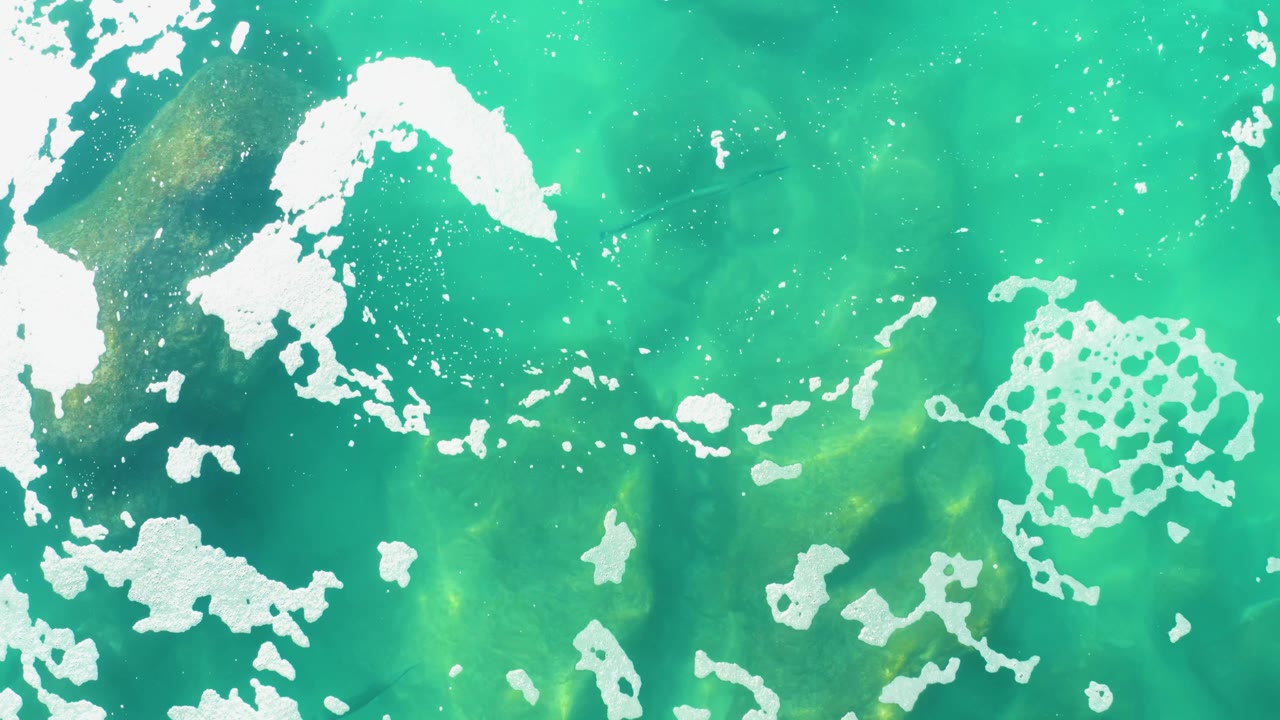 Clear turquoise water with white foam streaks and submerged dark areas.