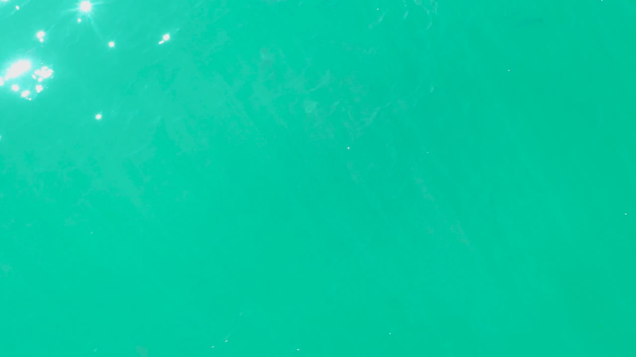 Turquoise water with bright sun reflections and faint fish below the surface.