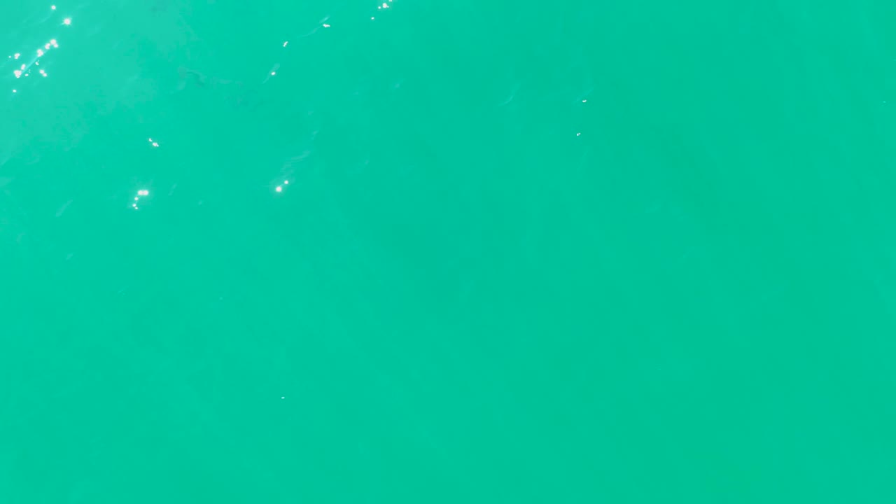 Overhead turquoise seawater at Laguna Beach Los Cabos shows clustered surface glare on the left and center, faint fish silhouettes below, and no visible people.