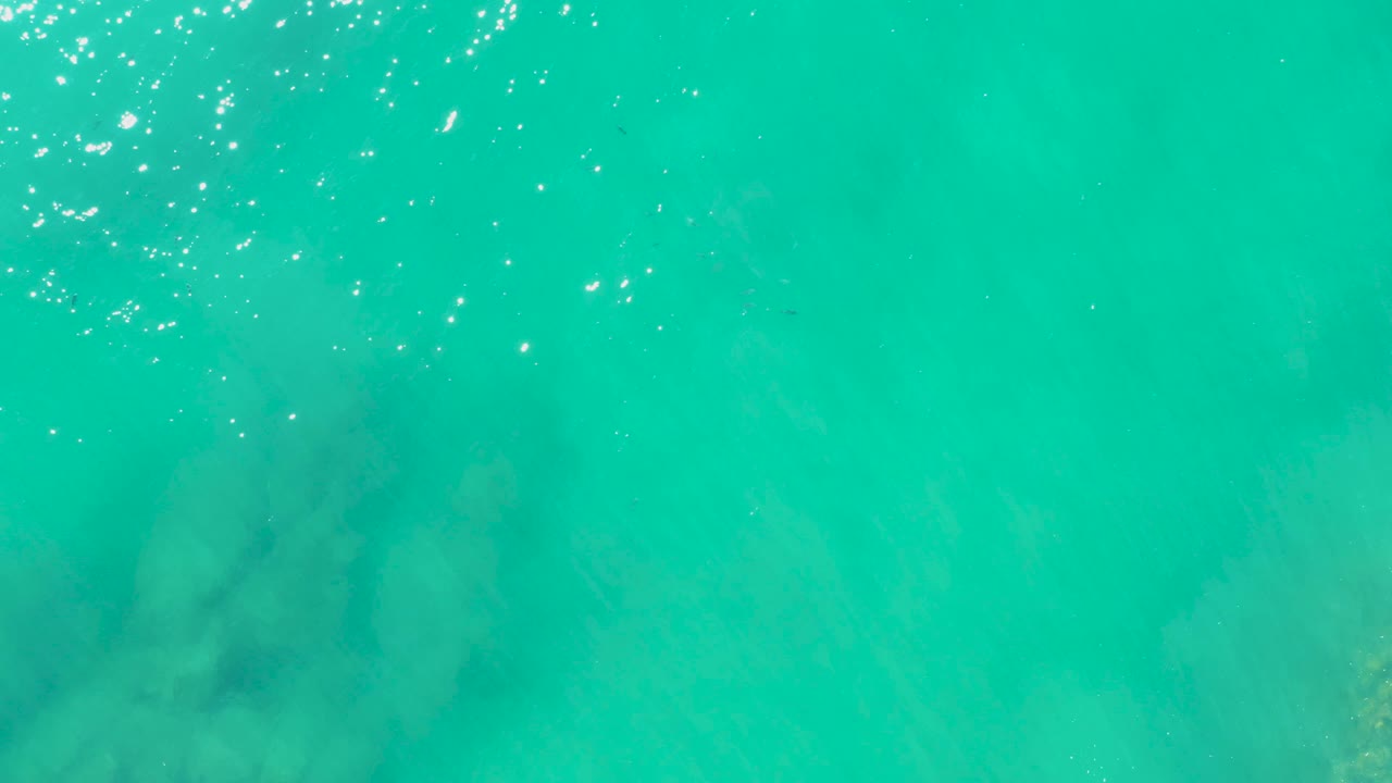 At 0:02, a darker cluster of underwater rocks sits beneath bright turquoise water in Laguna Beach Los Cabos, with rippled highlights near the top and no visible people.