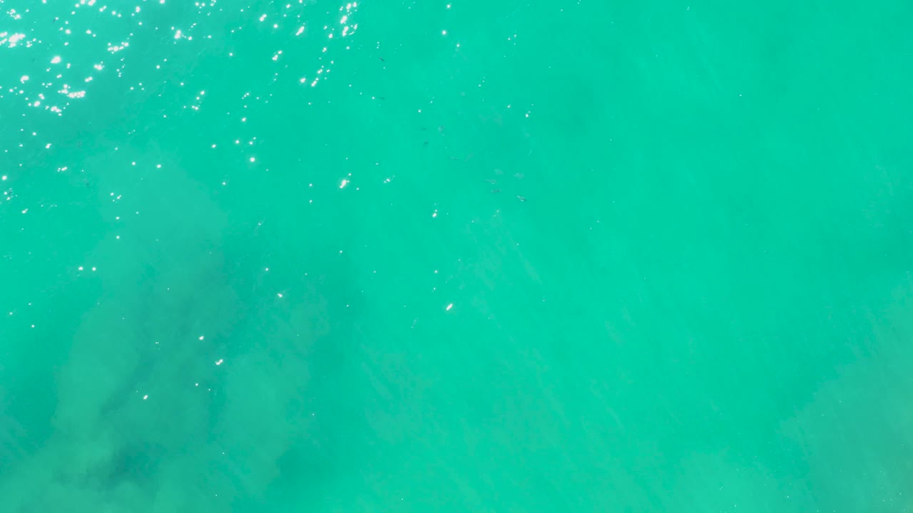 At 0:03, overhead turquoise water at Laguna Beach Los Cabos shows faint submerged rock shadows drifting toward the lower left of the frame, with no visible people.
