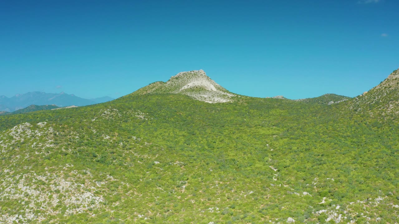 The mountain ridge remains centered beneath clear sky, showing green vegetation, pale exposed rock, and no visible people in the Laguna Beach Los Cabos landscape.