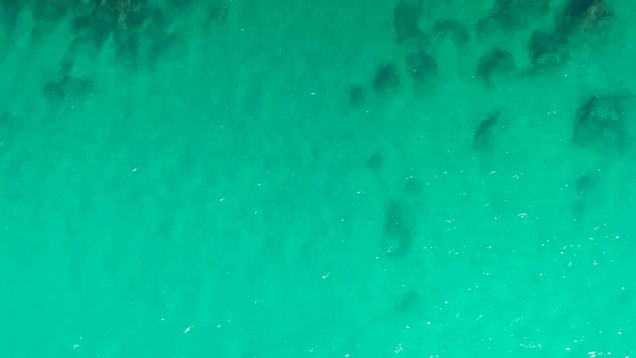 Turquoise water with dark underwater rock patches.