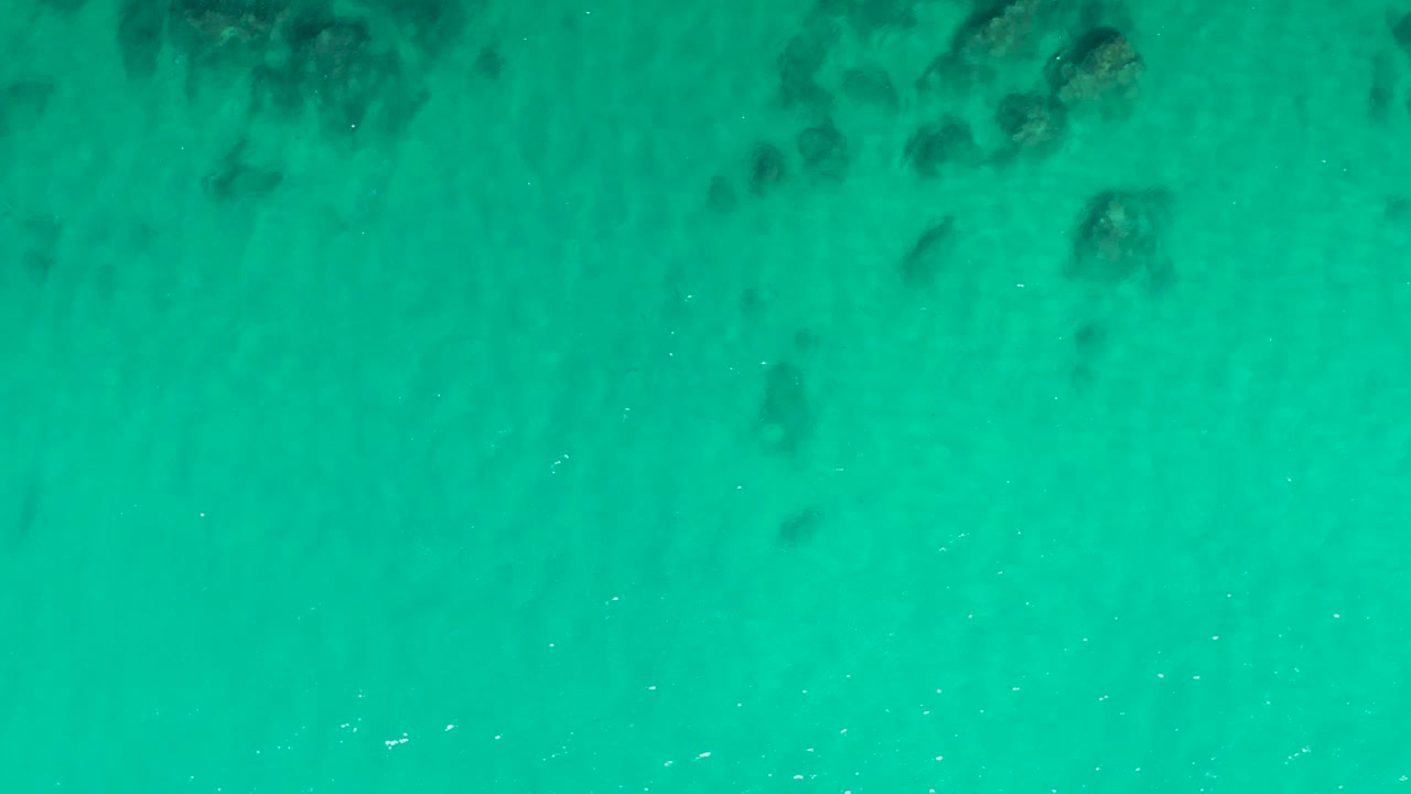 Turquoise shallow ocean water with dark submerged rocks.