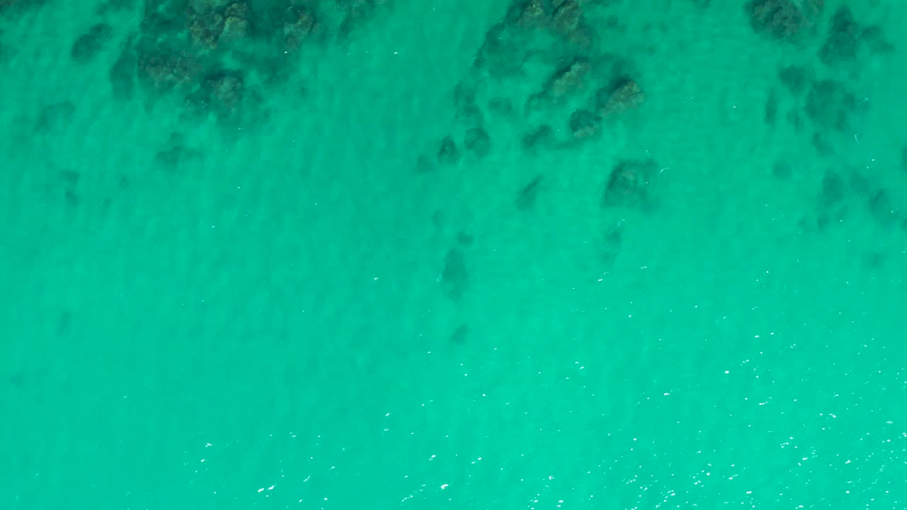 Turquoise water with dark submerged rocks near the top of frame.
