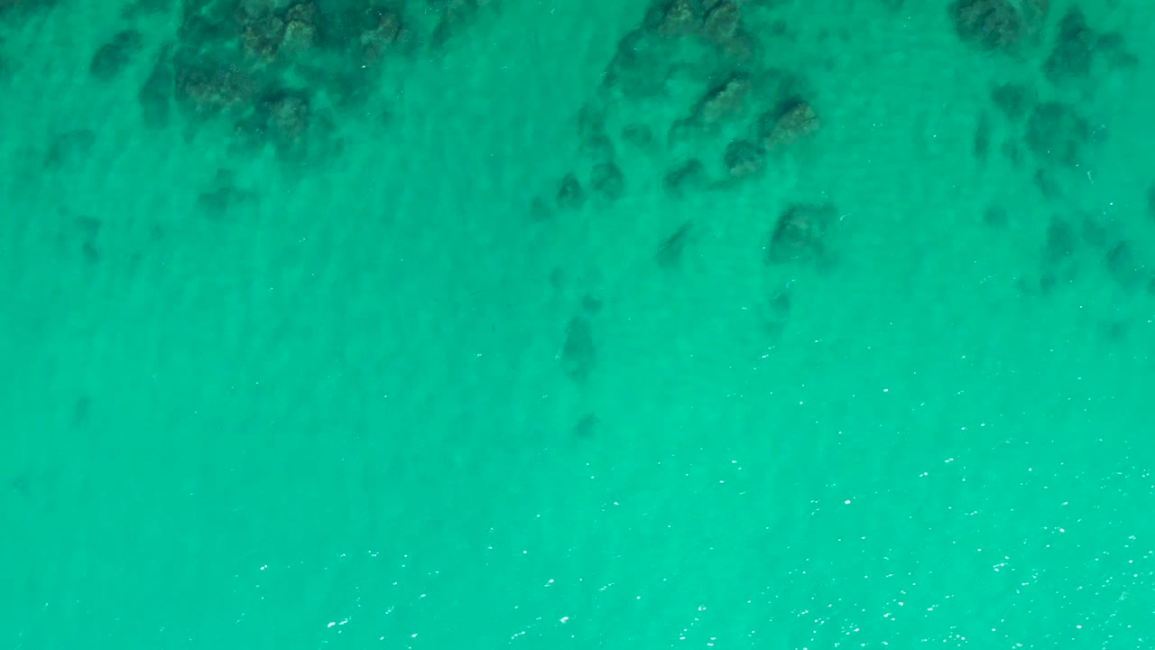 Clear turquoise ocean water at Laguna Beach Los Cabos shows shadowy rocks beneath the surface, faint ripple lines, and no visible people.
