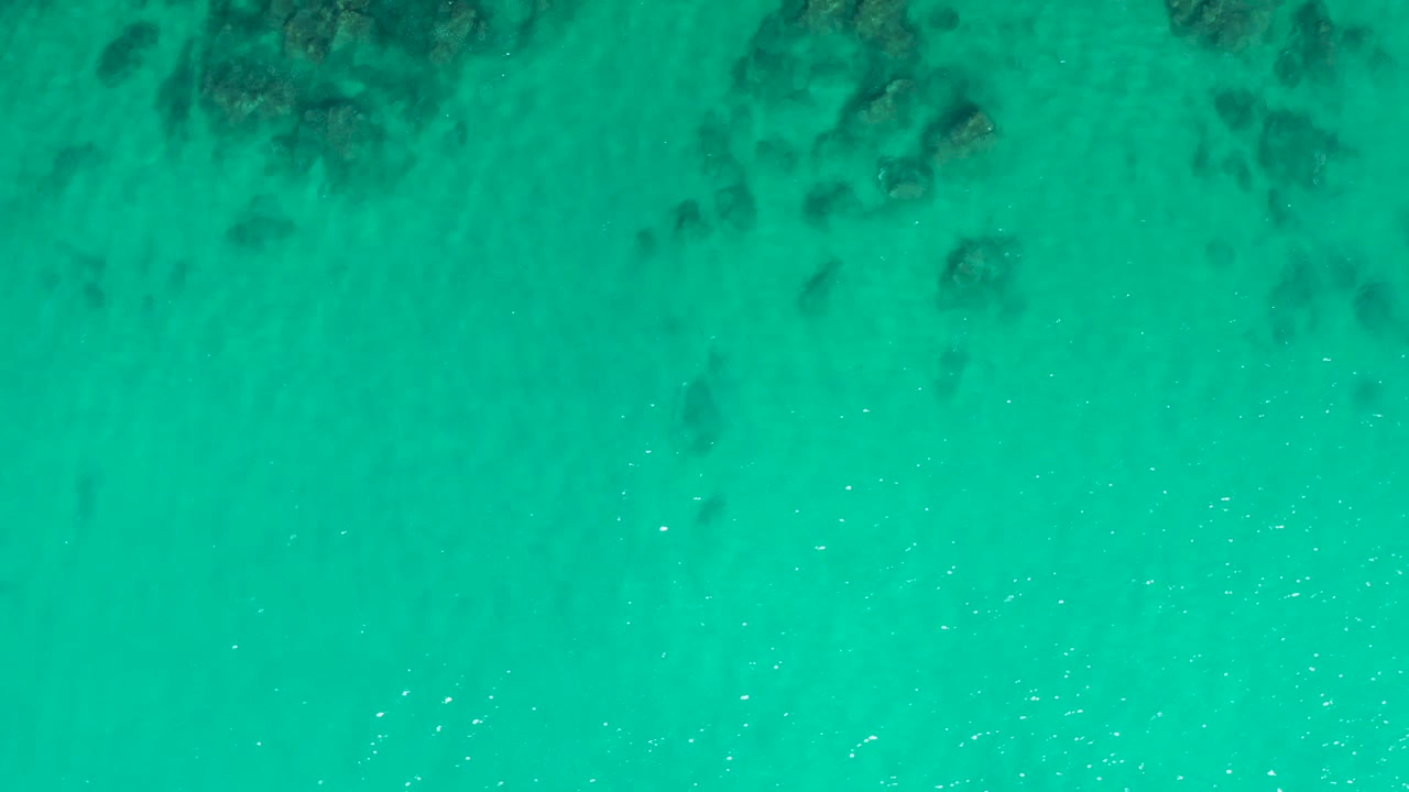 Aerial-style view of shallow turquoise water at Laguna Beach Los Cabos with scattered dark rock forms under the surface and no visible people.