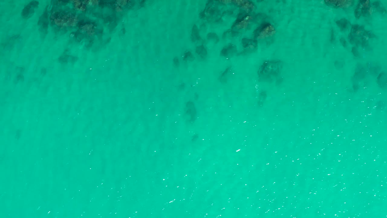 Transparent turquoise water at Laguna Beach Los Cabos reveals darker seabed patches through gentle surface texture, with no shoreline, boats, or visible people.
