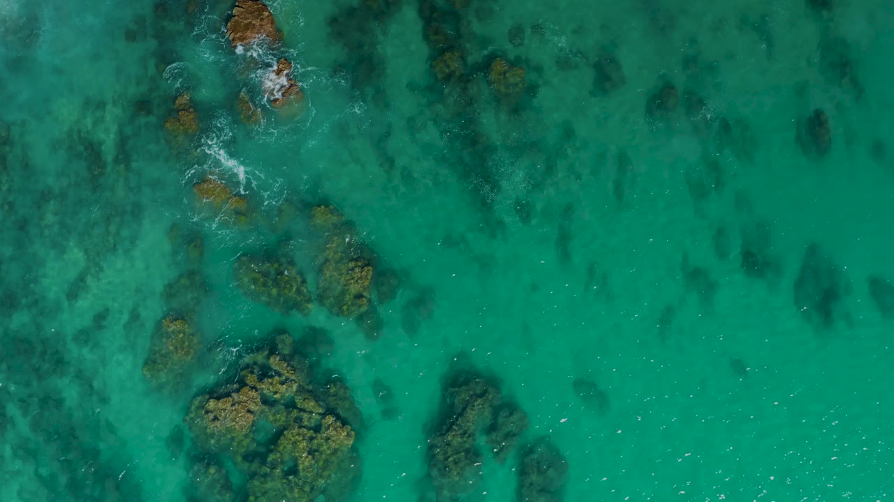 Overhead coastal water with rocky seabed and small surf breaks.