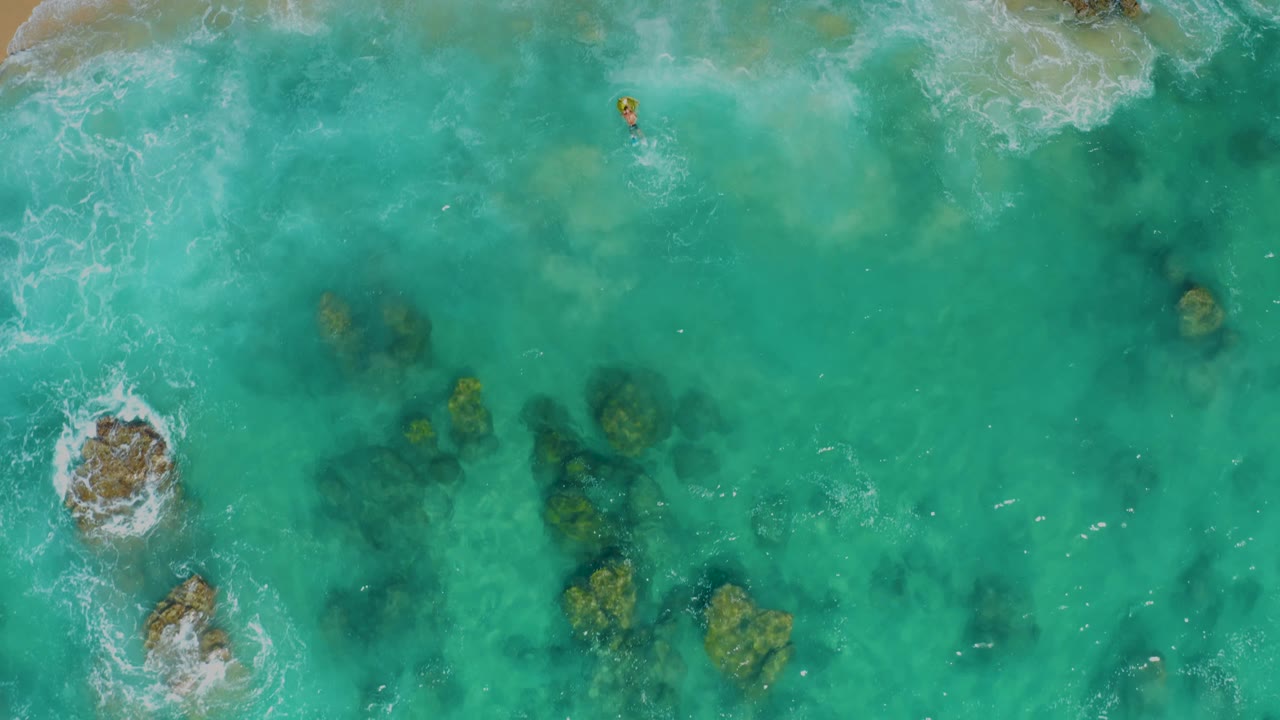 Overhead turquoise water with submerged rocks and small foam breaks.
