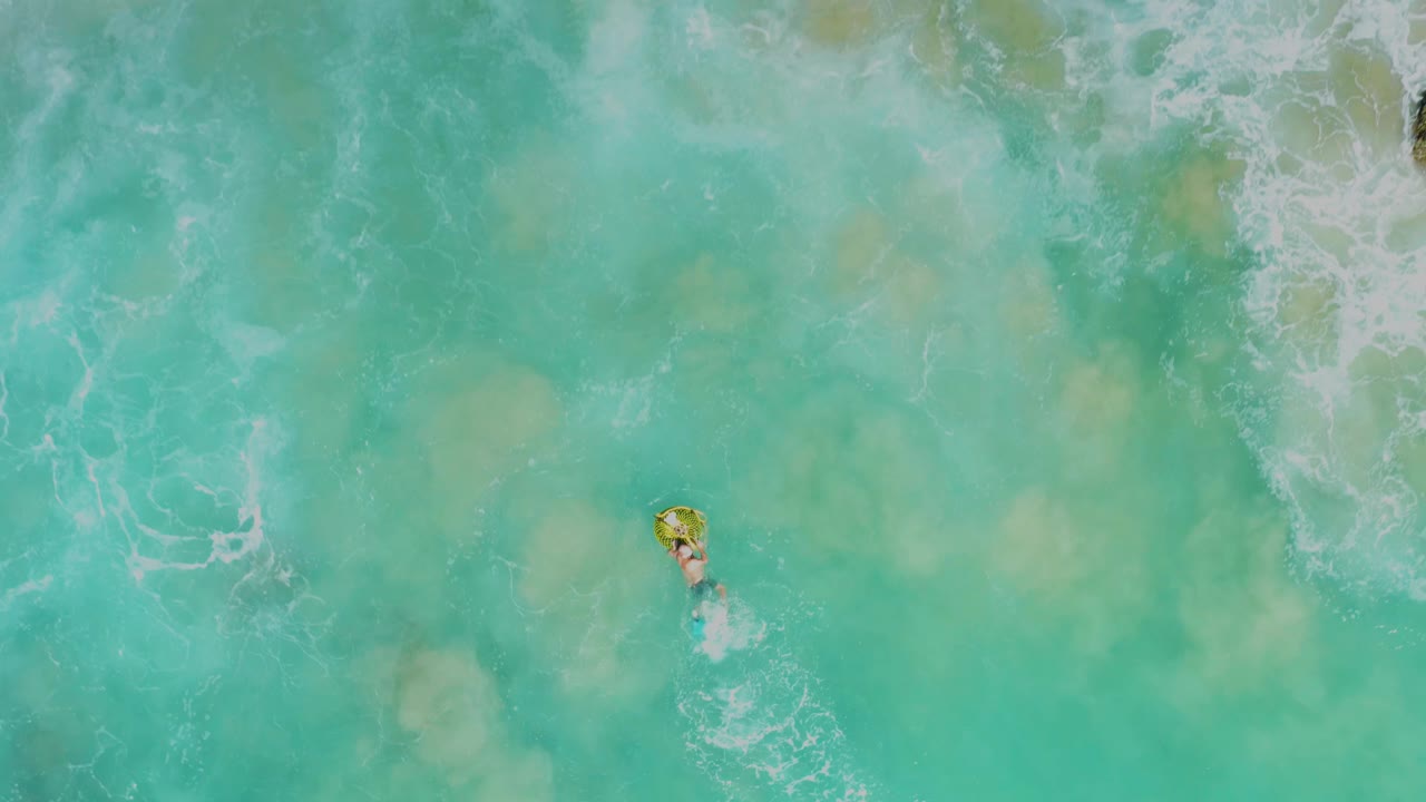 Person on a yellow float in clear turquoise water with white foam above.