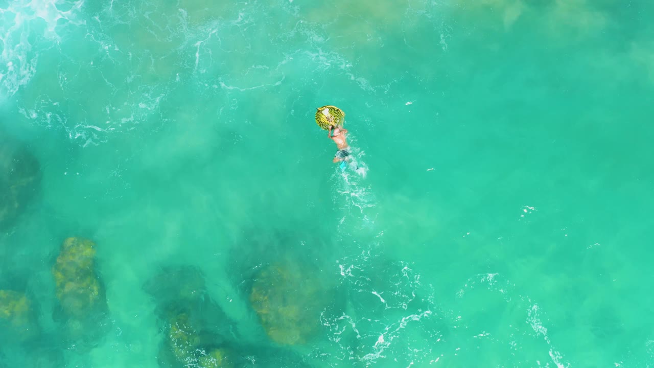 Swimmer holding a yellow ring above visible underwater rocks in clear ocean water.