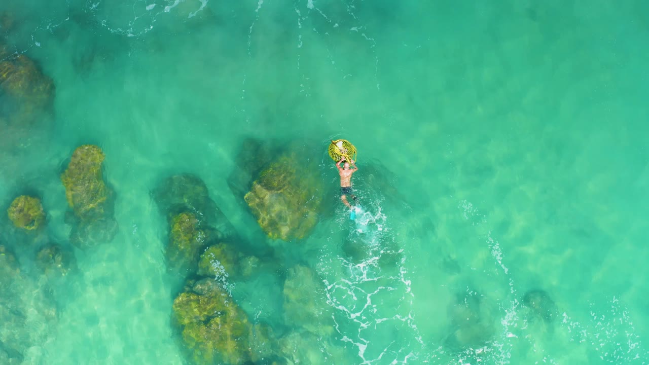 Person on a yellow float ring moving through clear turquoise water beside underwater rocks.