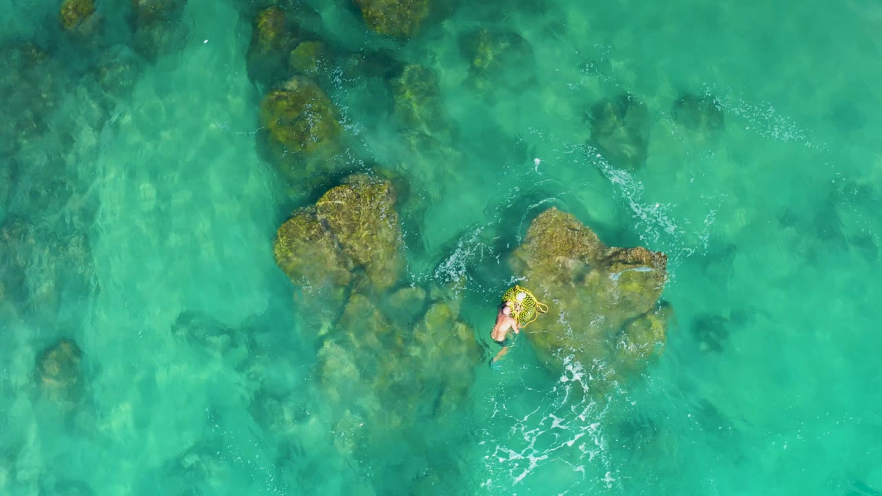 Overhead view at Laguna Beach Los Cabos of a swimmer near a large submerged rock cluster in clear turquoise water.