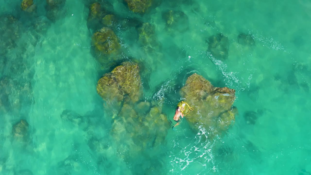 Swimmer moving past a rock cluster in clear turquoise sea.
