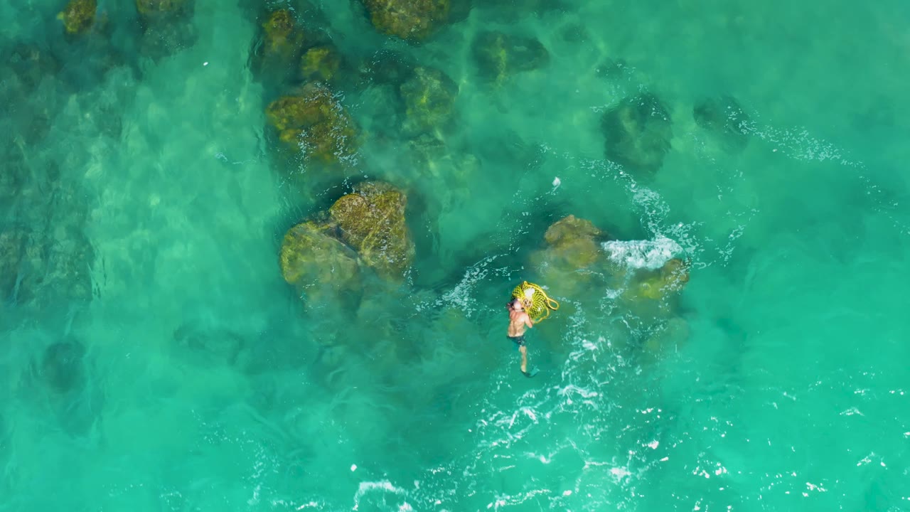 At 0:02, the swimmer has moved away from the larger rocks, leaving a small white wake in open turquoise water at Laguna Beach Los Cabos.