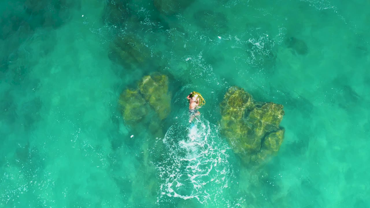 At Laguna Beach Los Cabos, the swimmer remains near the upper edge of the rock cluster while white water trails behind in the turquoise sea.