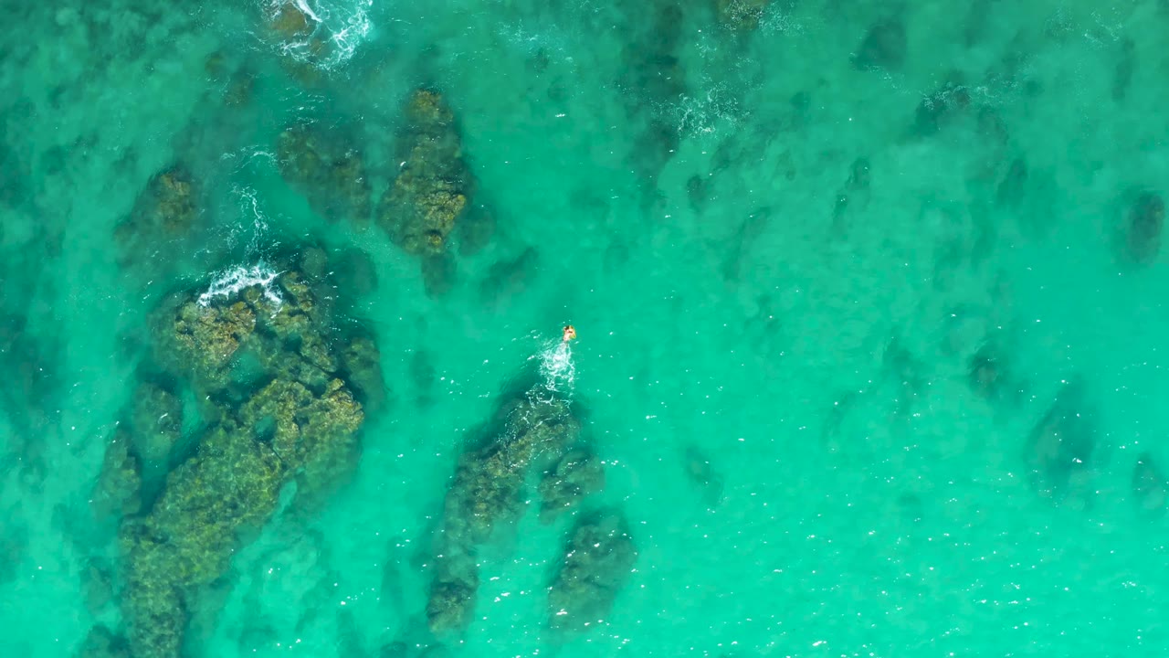 Clear green-blue water over rocks with a small person leaving a splash trail.