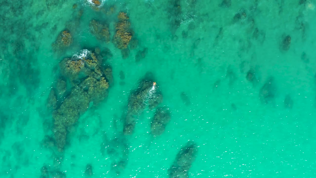Laguna Beach Los Cabos aerial view with a large rock mass on the left, smaller rocks to the right, white water touching the rocks, and no visible people.