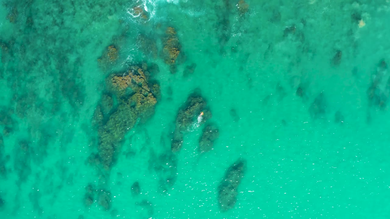 A larger submerged rock cluster appears left of center beneath clear turquoise water at Laguna Beach Los Cabos, with no visible people.