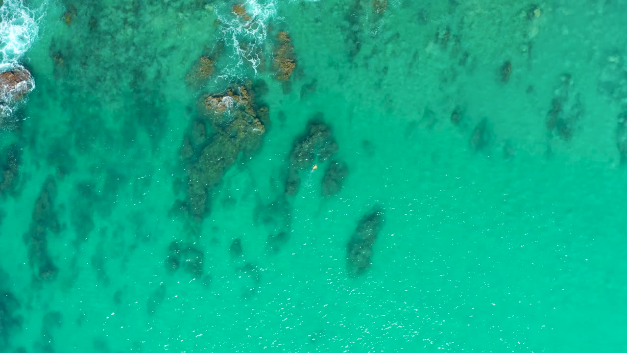 Overhead view at Laguna Beach Los Cabos with several submerged rocks grouped near the upper center, clear blue-green water around them, and no visible people.