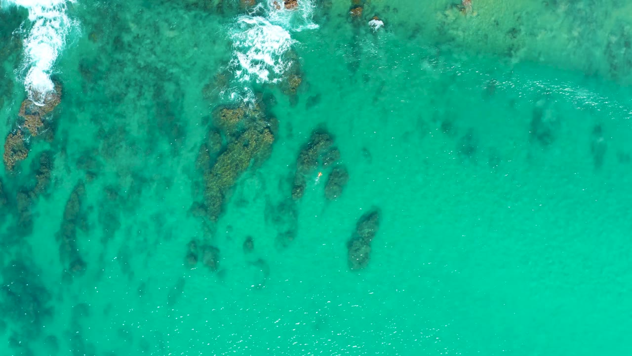 Clear turquoise water over rocks with a white foam patch near the upper left.