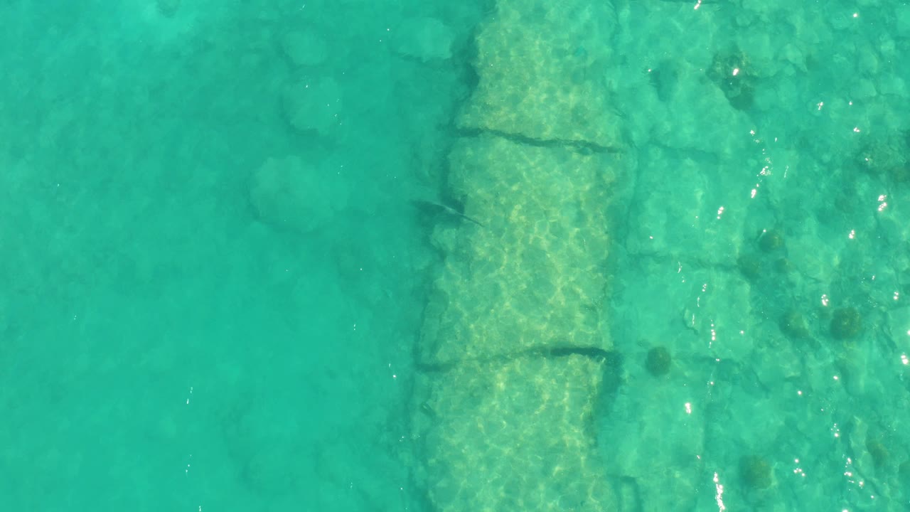 Overhead turquoise water with submerged stones and small fish