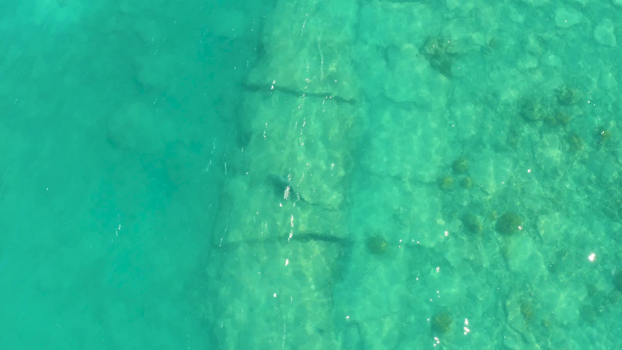 Cabo Pulmo overhead view showing the submerged stone form near the right side, with green-blue water, scattered rocks, and no visible people.