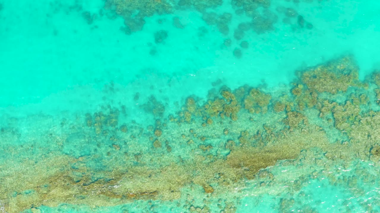 Clear turquoise water shows the seabed and a broad band of reef texture across the lower frame in Cabo Pulmo, Mexico, with no visible people.