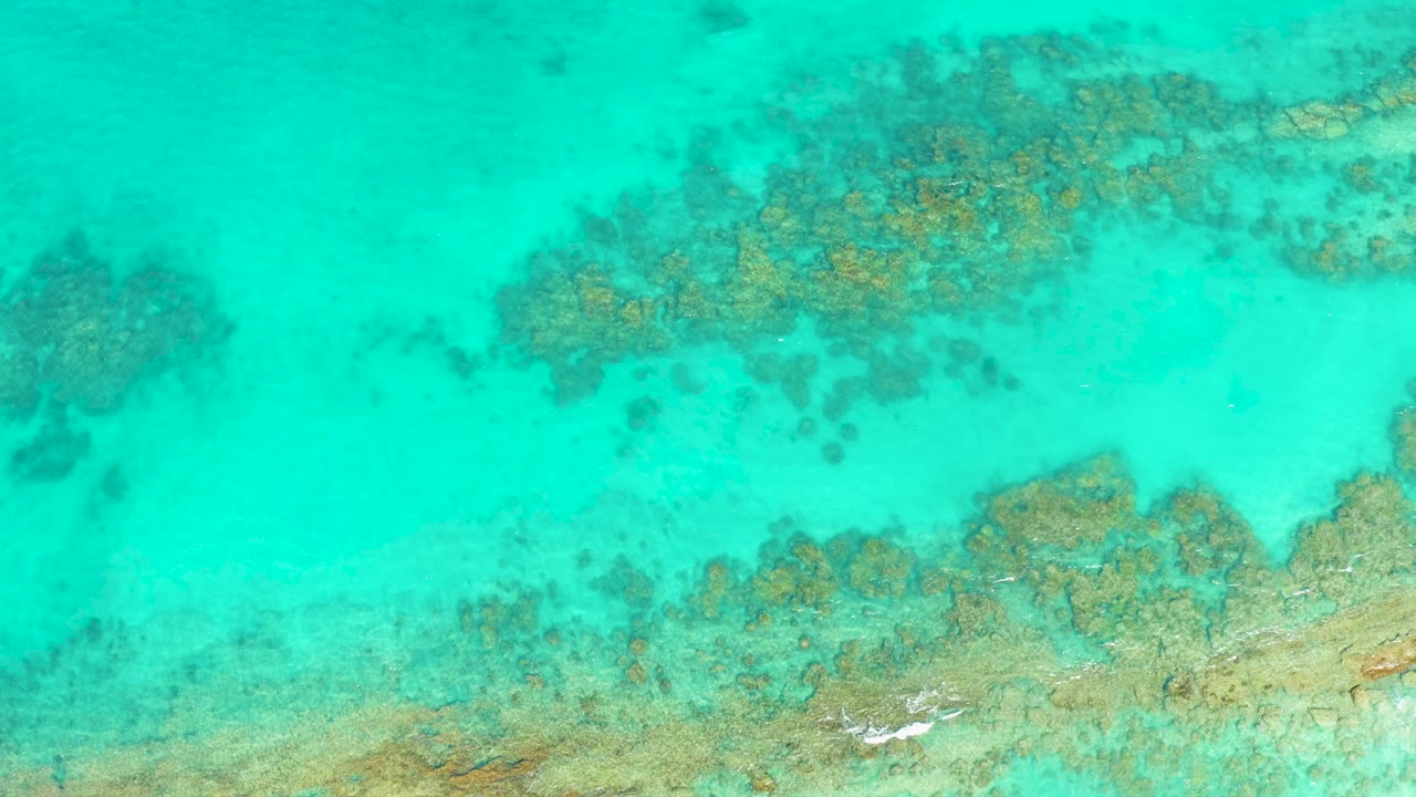 Overhead view of turquoise water in Cabo Pulmo with reef patches running across the top and lower edge, with no visible people.