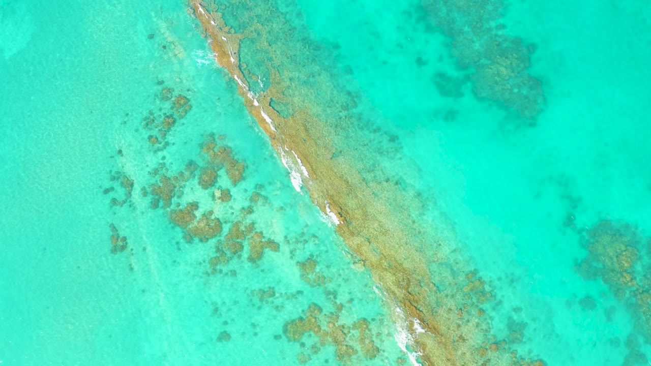 Diagonal sandbar under clear water with white foam along the edge.