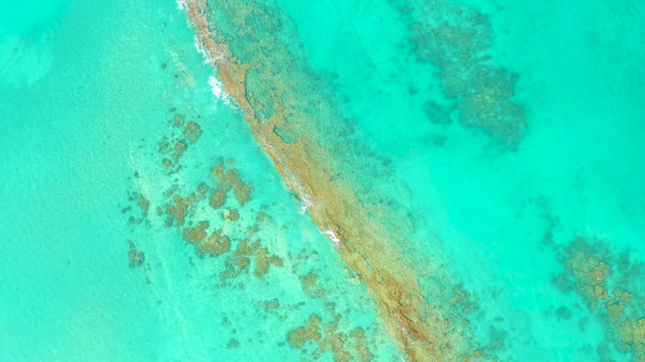 Cabo Pulmo aerial frame with the diagonal sandbar slightly shifted in the grid view, surrounded by aqua water, darker reef patches, and small foam touches, with no visible people.