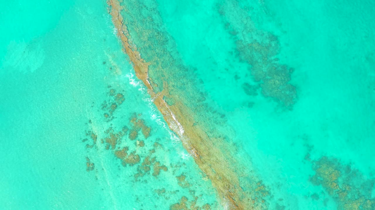 Overhead turquoise water with a diagonal sandbar and coral patches.