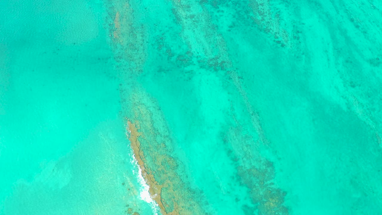 Overhead turquoise water with a narrow sandbar and foam on one edge.