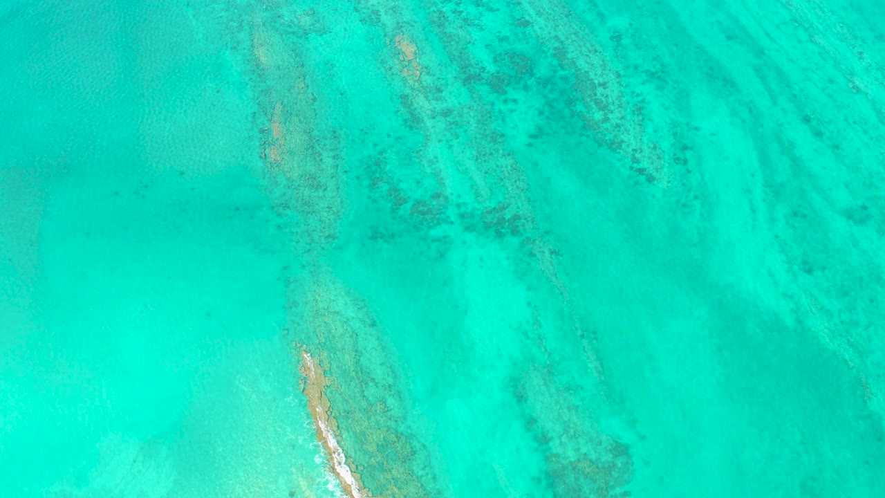 Shallow turquoise sea in Cabo Pulmo with pale sandy bottom, elongated reef streaks, and no visible people or vessels.