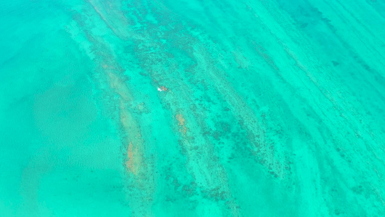 Overhead view of clear turquoise water in Cabo Pulmo with pale sand bands, darker underwater coral ridges, and no visible people.