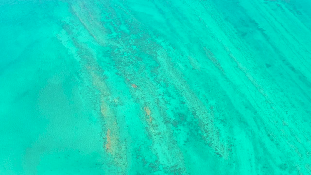 Clear turquoise water in Cabo Pulmo reveals diagonal sand bands and mottled darker seabed areas beneath the surface, with no visible people.