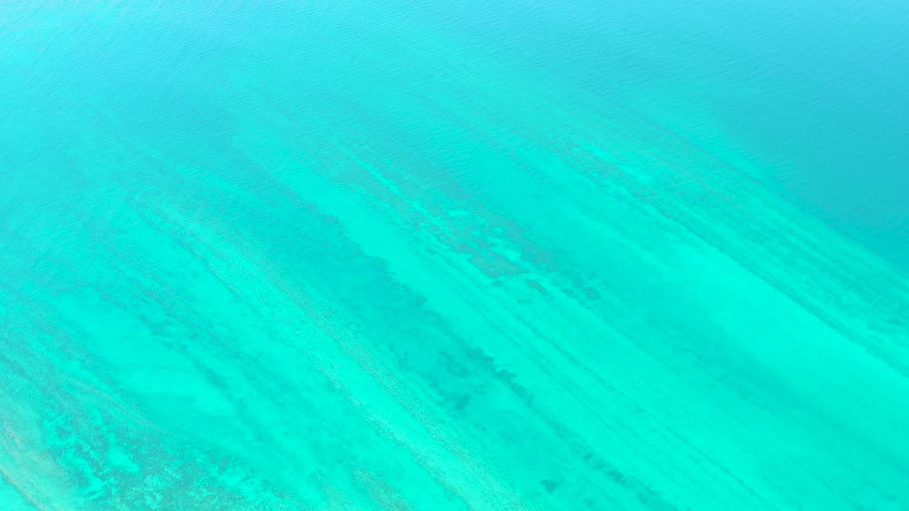 At one second, the Cabo Pulmo water remains bright turquoise, with diagonal sandy seabed bands and darker submerged marks visible beneath the surface, with no visible people.