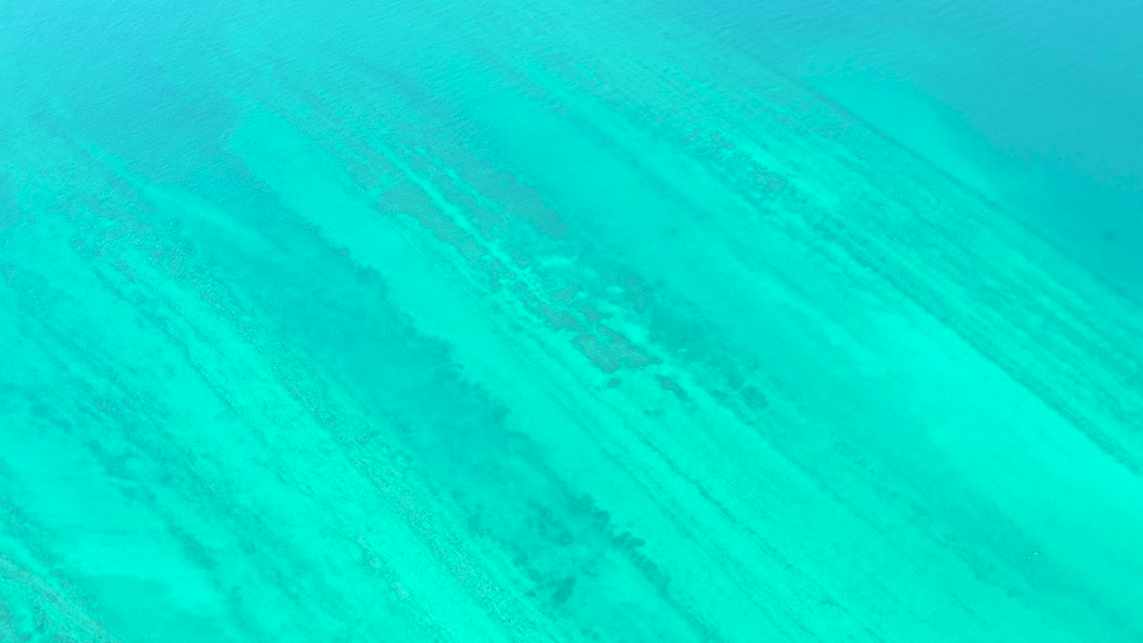 Clear turquoise water reveals diagonal seabed texture in Cabo Pulmo, with a slightly darker band crossing the frame and no visible people.