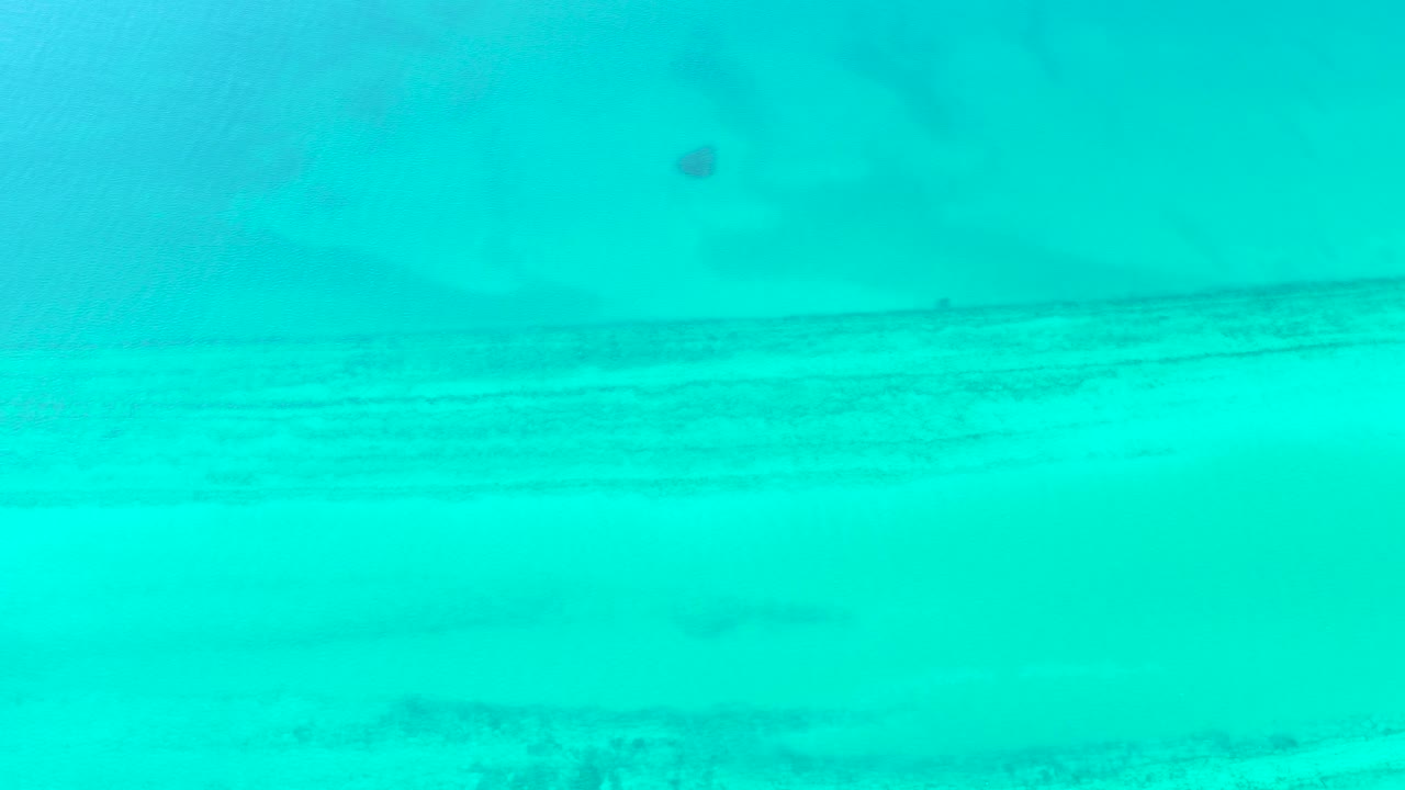 Second frame in Cabo Pulmo, Baja California Sur, with the sandy seabed still visible beneath translucent turquoise water and a slightly shifted ripple pattern, no visible people.