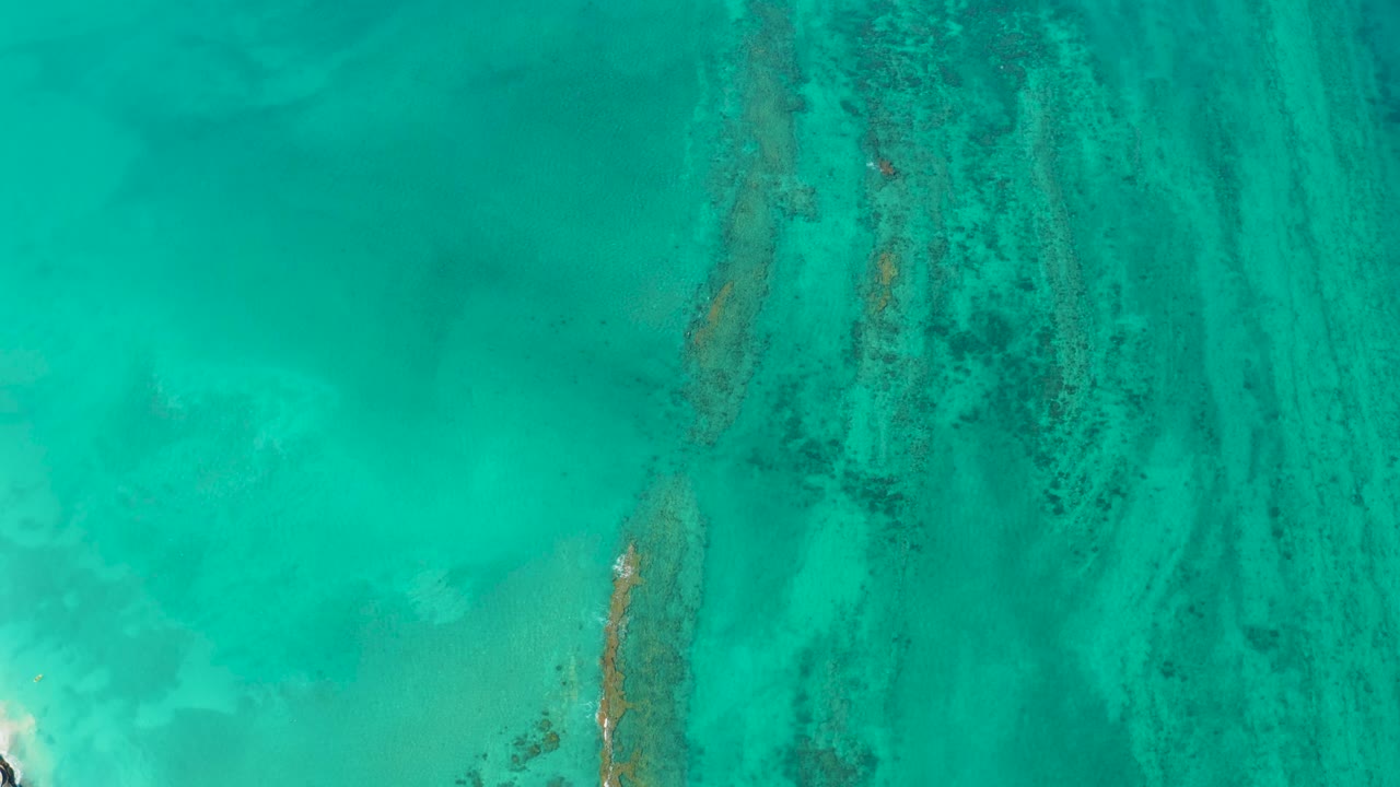 Clear turquoise sea in Cabo Pulmo shows long darker reef lines running through pale underwater sand, no visible people.